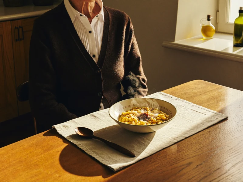 Tavolo di cucina illuminato dal sole con una minestrina fumante e cucchiaio di legno